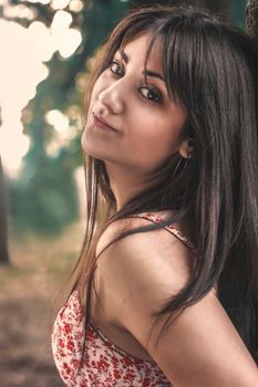A beautiful woman with long brunette hair posing outdoors, wearing a floral top.