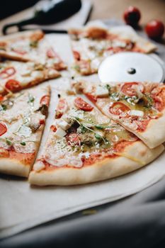 Close-up of a sliced pizza with various toppings and a pizza cutter on a table.