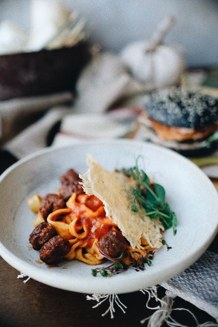 A white bowl of spaghetti tossed in marinara sauce topped with meatballs and grated parmesan, with a basket of warm breadsticks beside it.