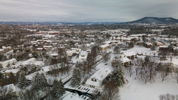 Aerial view of snow-covered State College, Pennsylvania, showcasing rooftops and landscapes in winter.