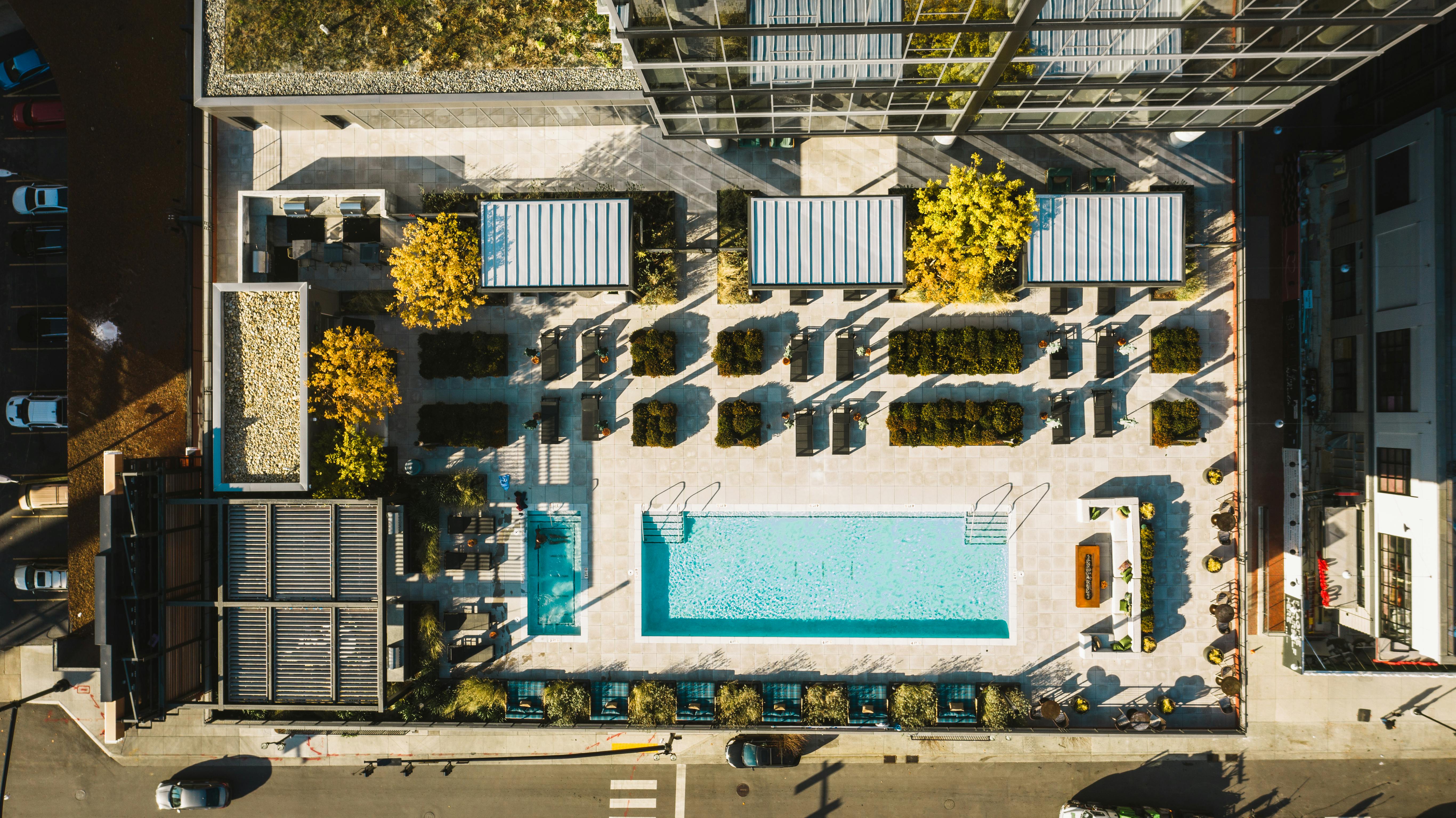 Aerial view of a contemporary rooftop pool and patio area with lounge chairs and greenery.