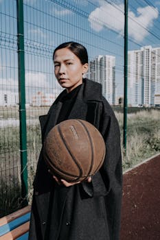 Stylish woman holding a basketball in an urban outdoor setting.