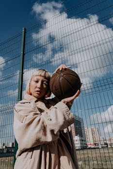 Fashionable woman holding basketball outdoors against a city backdrop.