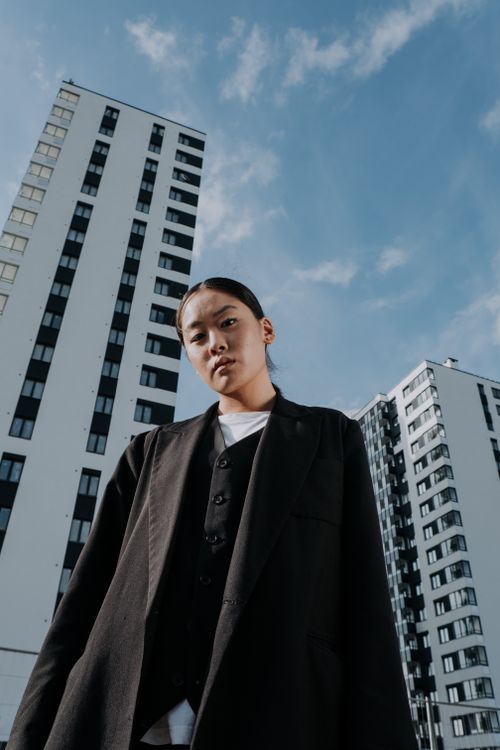Free Stylish woman in fashionable attire stands confidently against an urban cityscape backdrop, showcasing modern architecture. Stock Photo