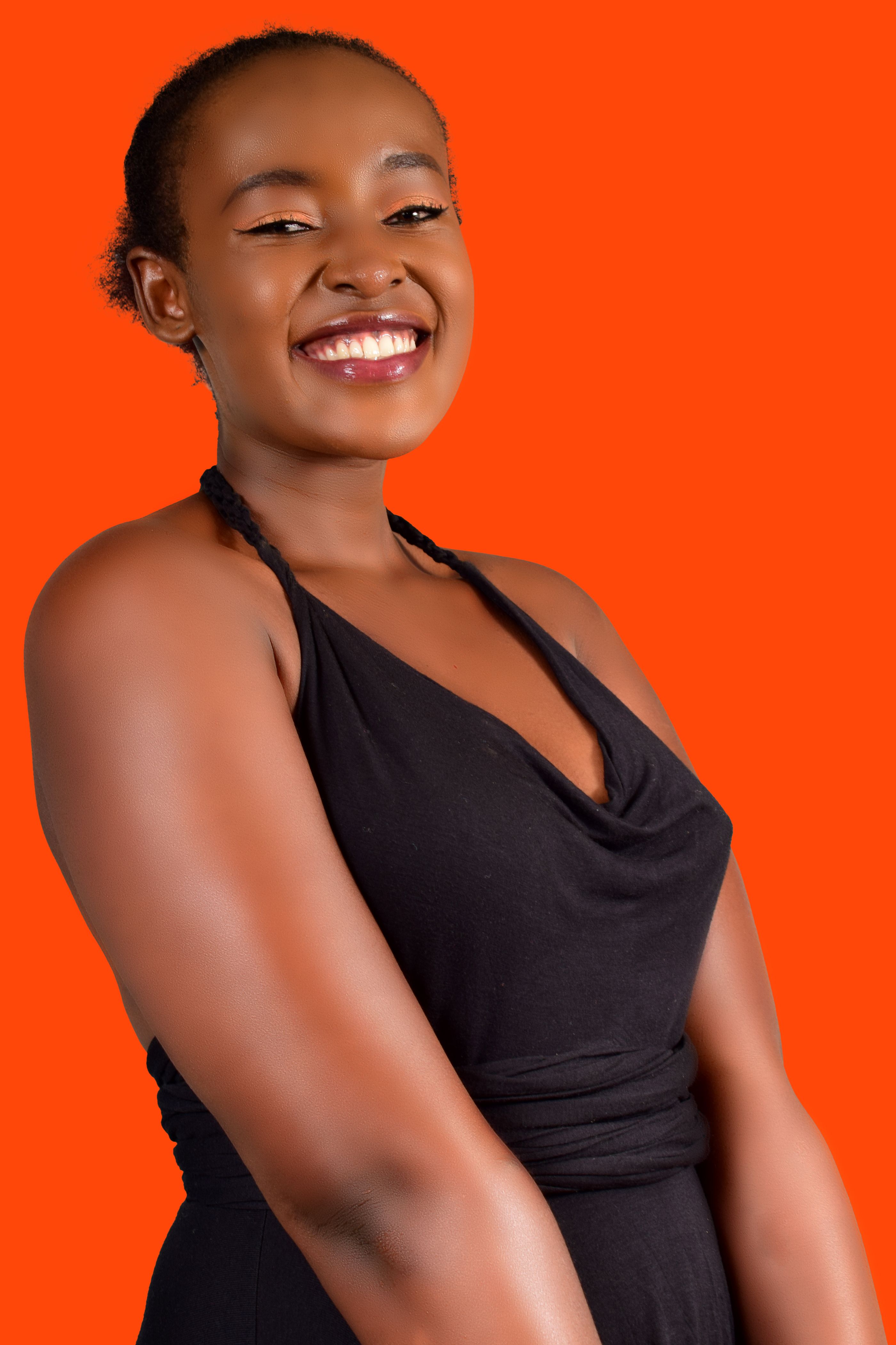 Cheerful woman in a black dress against a vibrant orange background, smiling warmly.