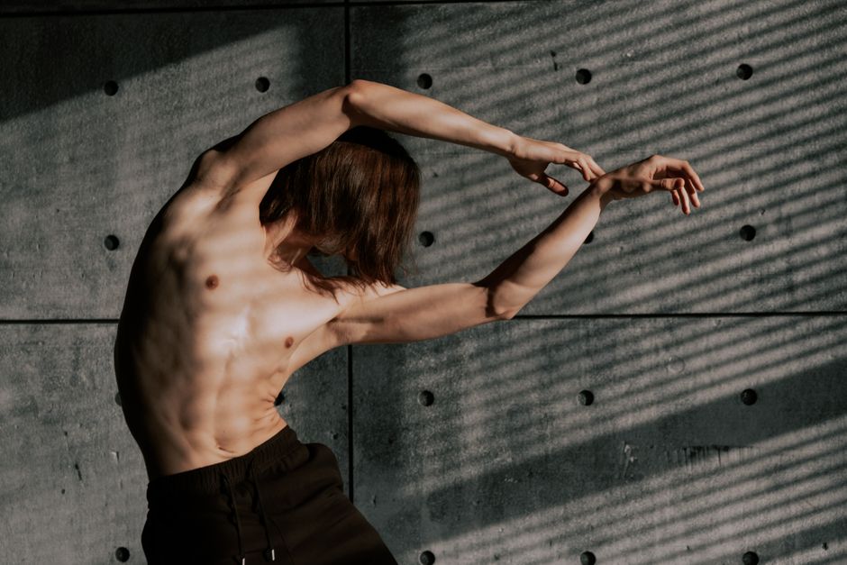 Shirtless male dancer showcasing fluid movement against a textured concrete wall.