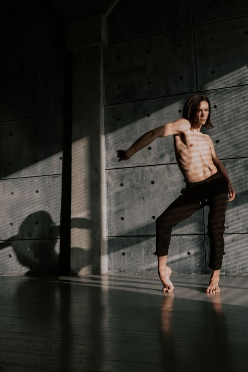 Free Shirtless male dancer striking a pose with dramatic shadows indoors. Stock Photo