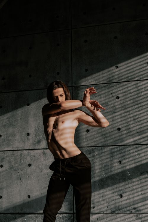 Free A contemporary dancer performs a shirtless acrobatic pose against a textured wall, showcasing grace and flexibility. Stock Photo