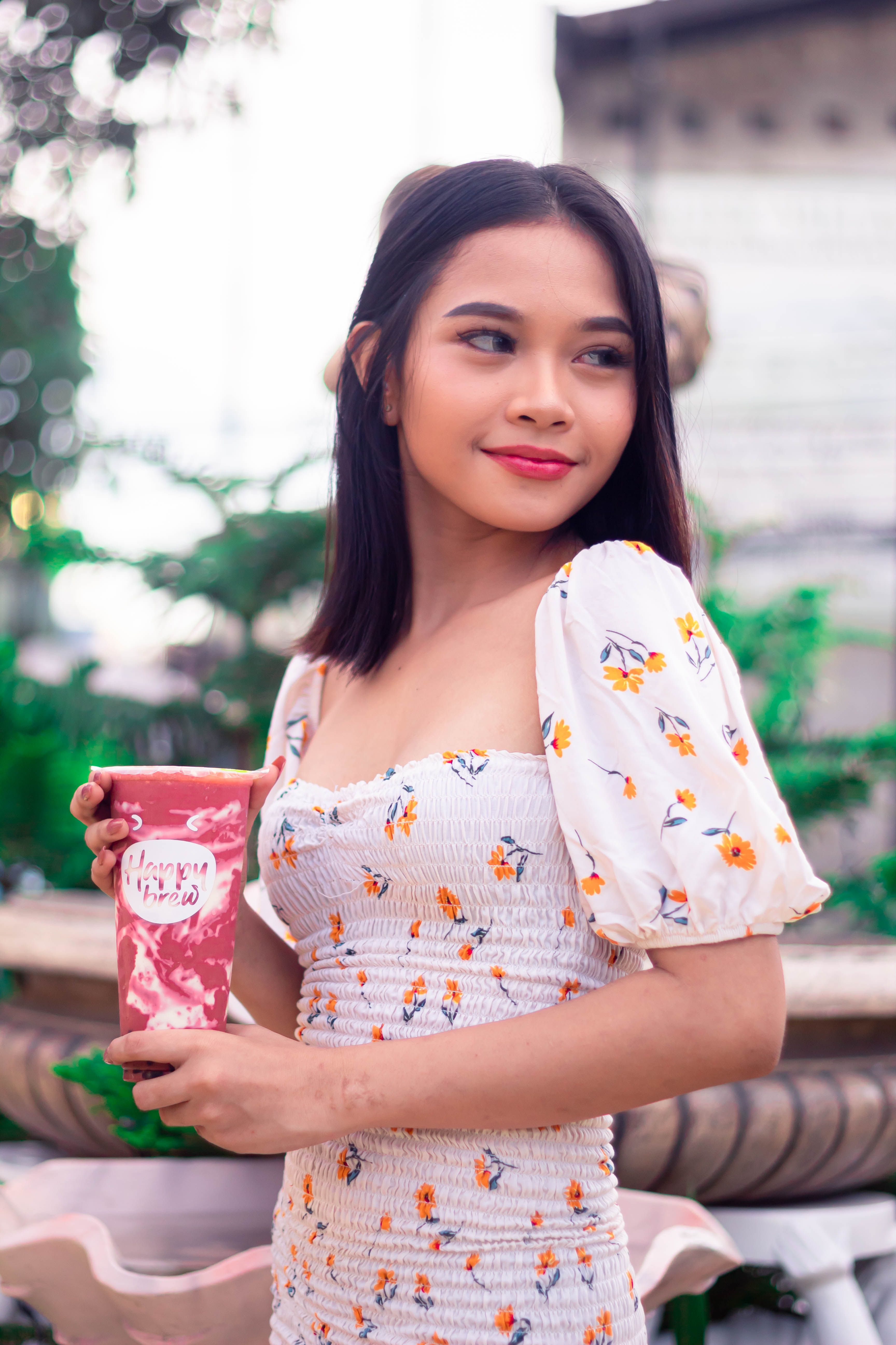 Smiling woman in floral dress holding a decorative cup outdoors.