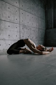 Male dancer performing a contemporary pose against a concrete wall, showcasing flexibility and grace.