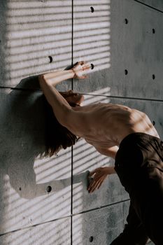 Artistic shot of a flexible dancer with a bare torso leaning against a textured wall.