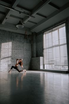 Woman dancing in spacious sunlit industrial studio, showcasing movement and grace.
