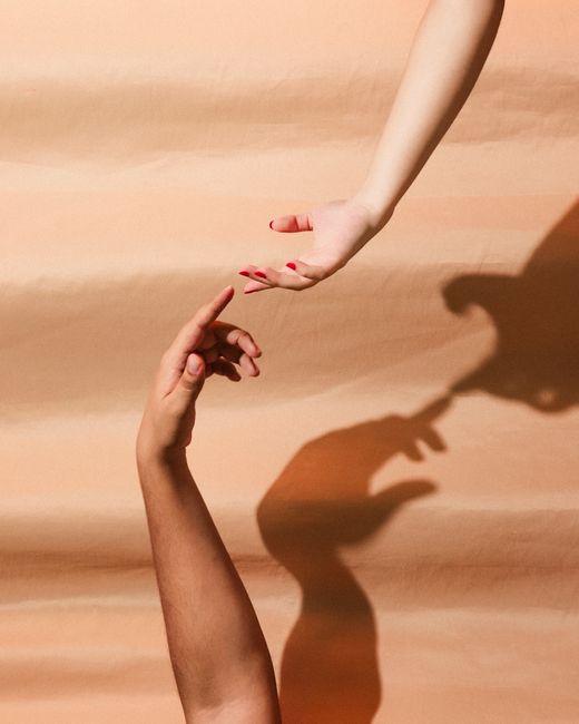 A conceptual minimalist image of two hands reaching towards each other with shadows on a peach background.