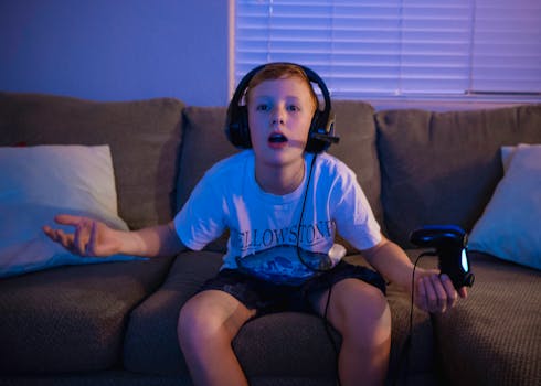 A young boy sitting on a couch, wearing a headset, playing video games indoors.