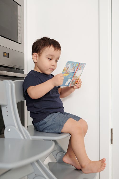 Boy in Blue T-shirt Sitting on Plastic Chair Reading A Book