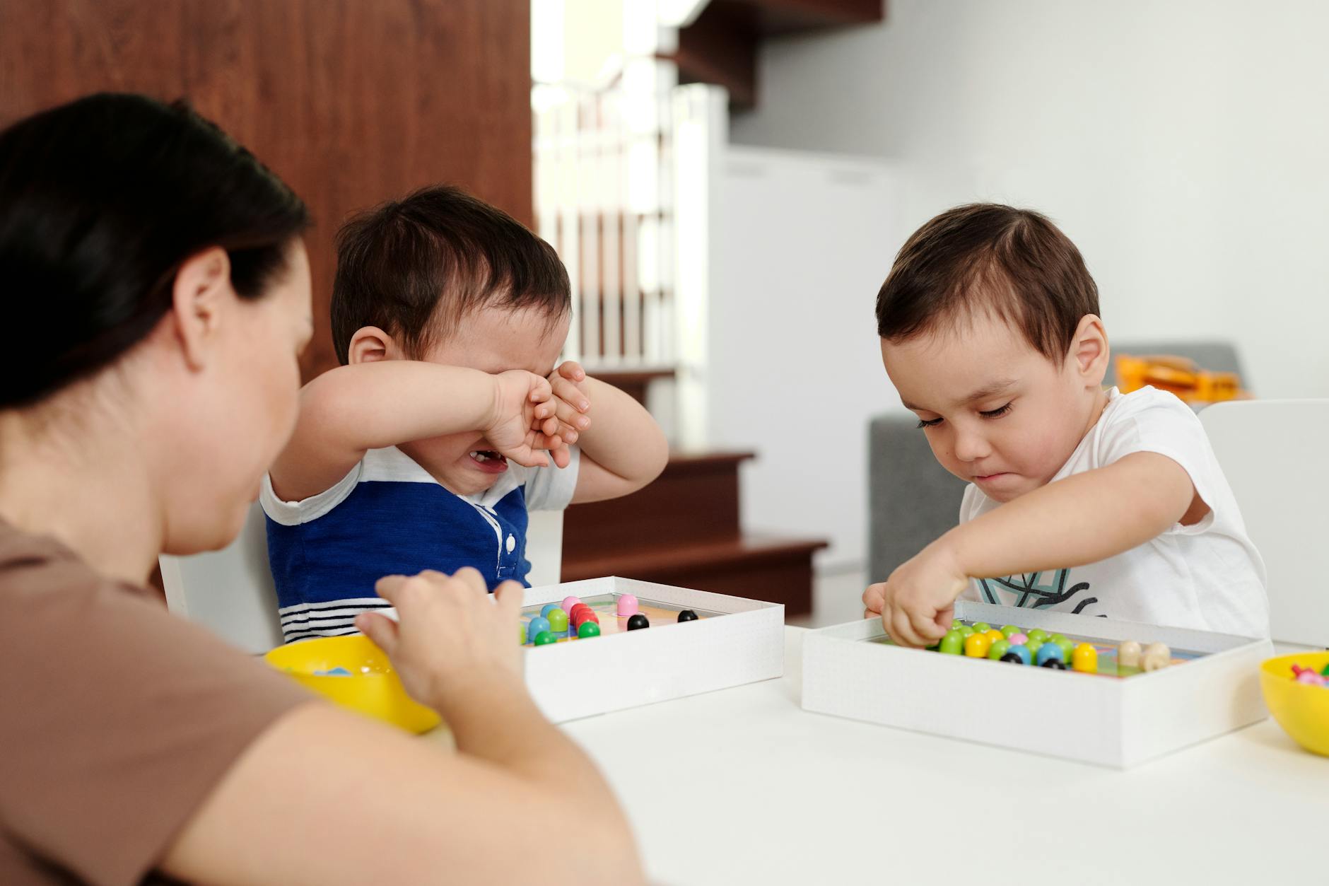 Mother supervising children playing with colorful beads indoors, promoting creativity and family bonding.