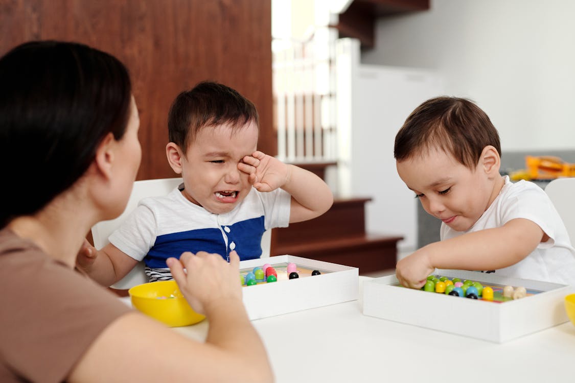 Free Woman Playing with Two Children and One Child Crying Stock Photo