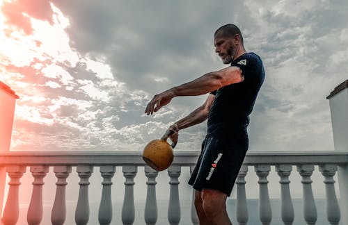 Man in Black Shirt Carrying Kettle Bell Outdoors