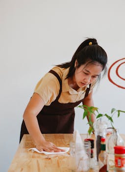 Asian woman wiping a wooden table in a restaurant, showcasing small business operations.