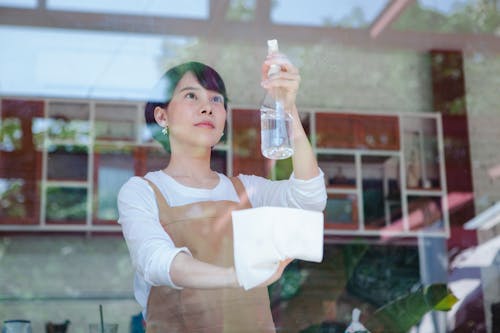 Free Asian woman wiping glass with a spray bottle and cloth, inside a restaurant setting. Stock Photo