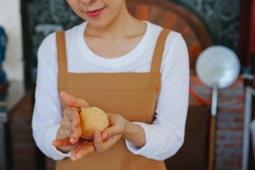 Person Wearing Brown Apron Holding a Dough