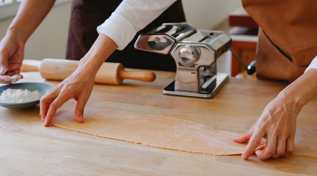 Hands preparing fresh pasta dough with a pasta maker on a wooden surface.