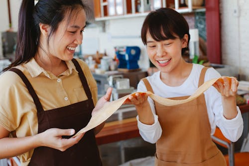 Women Wearing Brown Aprons Holding a Dough Together