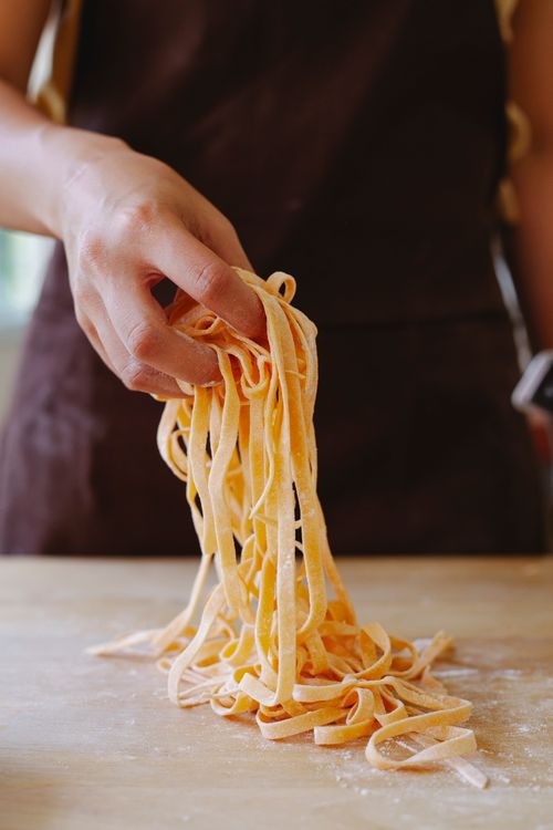 Free A close-up image showcasing a hand holding fresh uncooked pasta on a wooden surface. Stock Photo