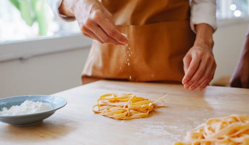 Person Sprinkling Flour on Pasta