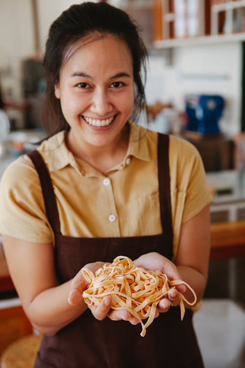 Photograph of a Woman in a Brown Apron Showing Pasta while Smiling