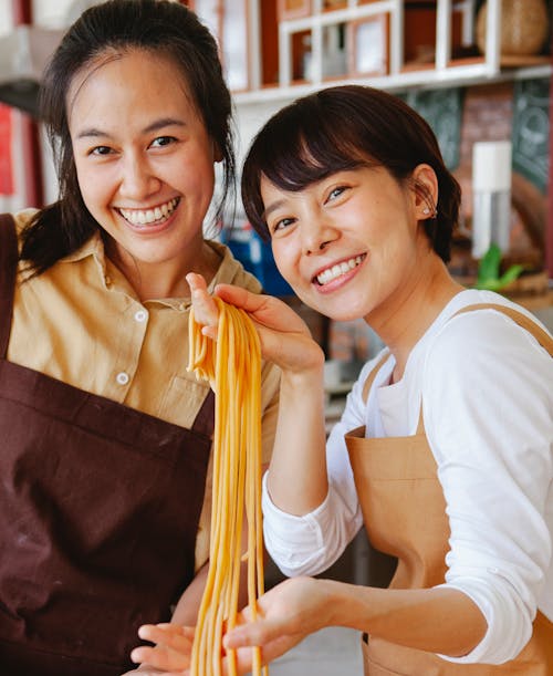 Photo of Two Women Showing Pasta while Smiling