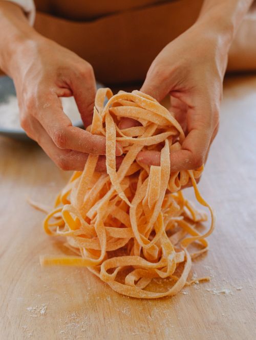 Free Close-up of hands holding homemade raw pasta on a wooden table. Perfect for cooking and food concepts. Stock Photo