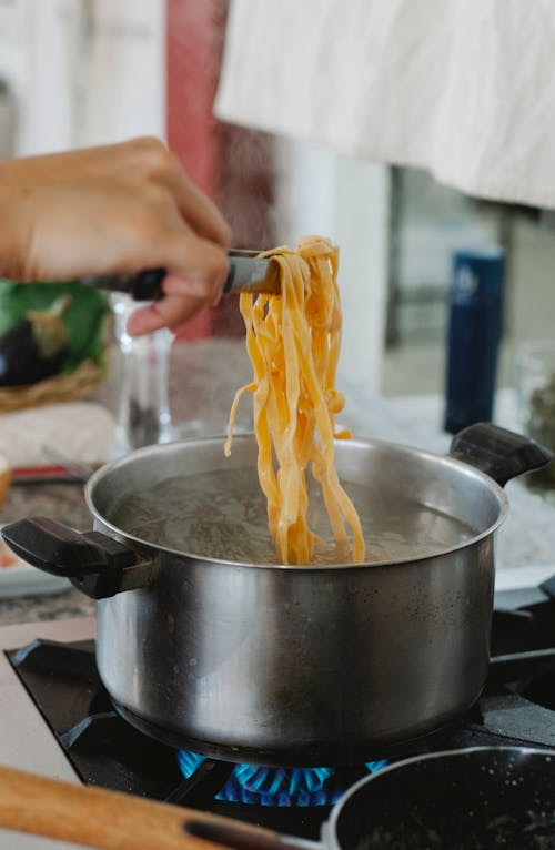 Person Taking Pasta Out of the Boiling Water 