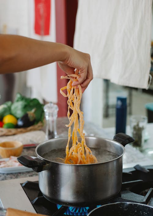 Hand Holding Pasta over Pot