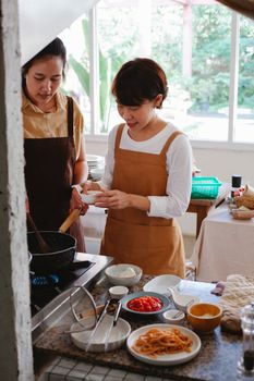 Two women preparing a meal together in a sunlit kitchen, wearing aprons and surrounded by ingredients.