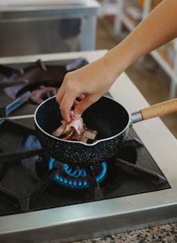 A hand placing meat in a frying pan over a stove flame. Perfect for cooking and culinary concepts.