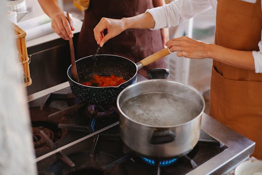Close-up of two women cooking; stirring sauce and boiling water on stove.