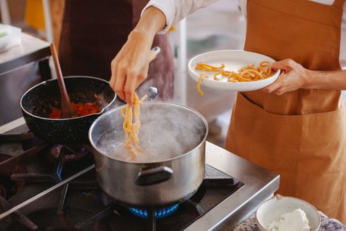 Free Close-up of a person cooking fresh pasta on a stove with sauce preparation. Stock Photo
