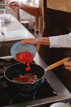 Chef adding chopped tomatoes to a stir fry pan on a stove for a delicious meal.
