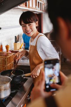 Happy woman wearing an apron cooking while being photographed in a modern kitchen.