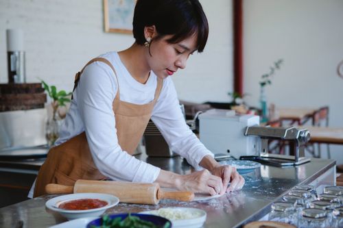 Free A woman in an apron kneads dough on a stainless steel counter in a modern kitchen setting. Stock Photo