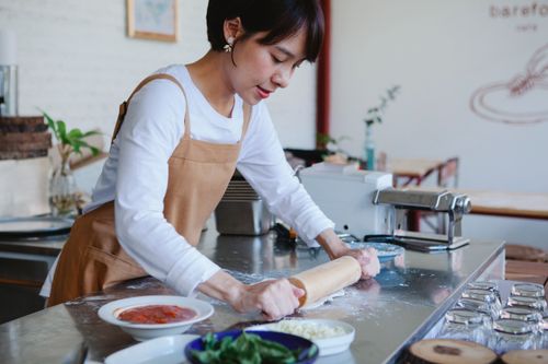 Free Woman in apron kneading dough on a kitchen counter with ingredients nearby, showcasing food preparation. Stock Photo