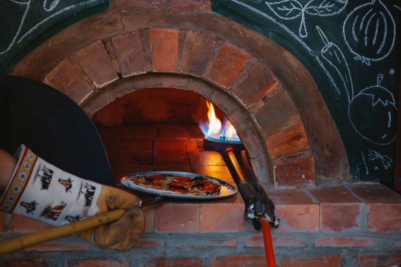 Pizza wird auf dem Schieber in den flammenden Holzofen geschoben