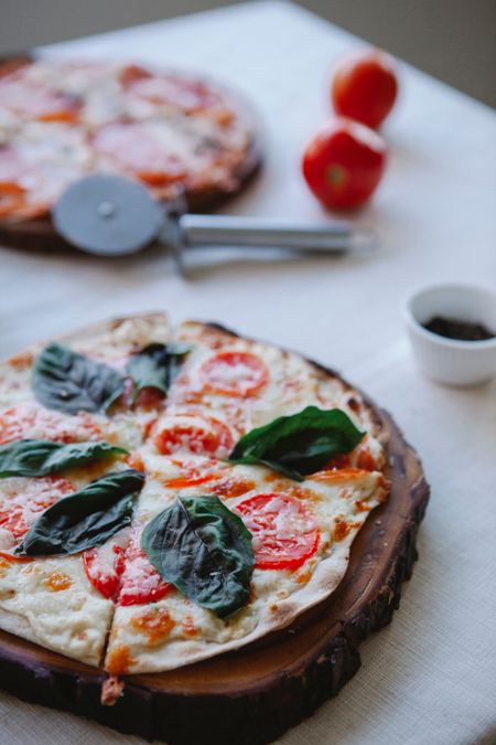 Fresh basil and tomato pizza on a wooden board, photo by Antonius Ferret on Pexels