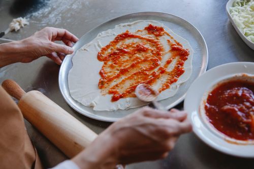 Free A detailed view of spreading tomato sauce on pizza dough, ready for baking. Stock Photo