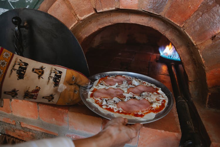 Hand Of A Person Placing Pizza On Aluminum Plate In Oven