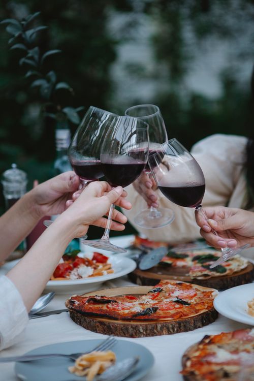 Free Adults toast with red wine glasses over a pizza dinner, symbolizing friendship and celebration. Stock Photo
