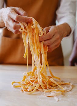 A person carefully handling freshly cut uncooked pasta strands in a kitchen setting.