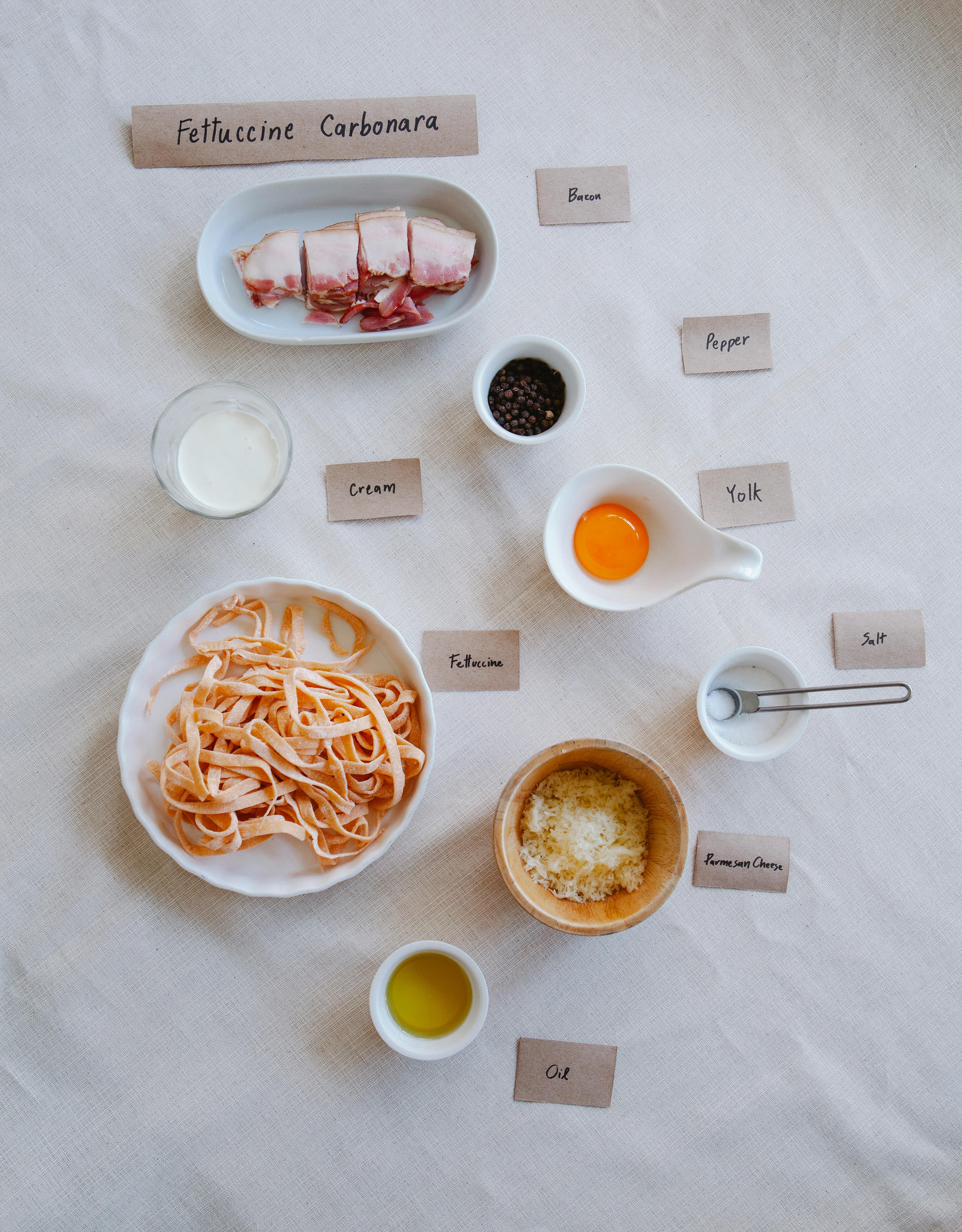 Flat lay of fettuccine carbonara ingredients including bacon, cream, and Parmesan cheese.
