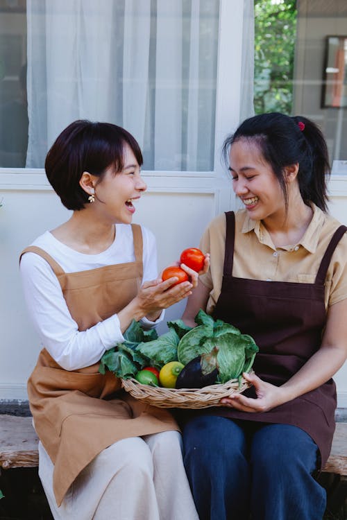 Two Women Sitting While Holding a Woven Basket of Fresh Vegetables